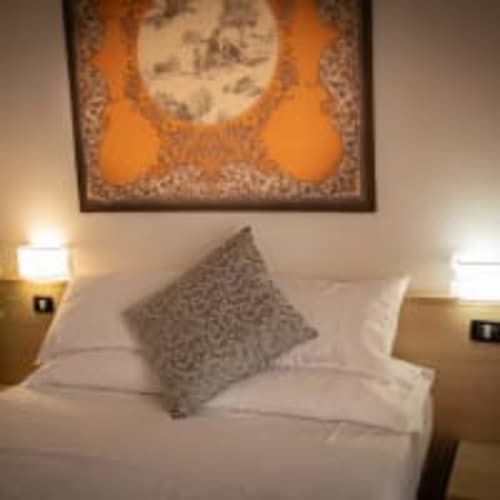 Accogliente camera all'Hotel Vista Lago a Brunate con letto bianco, cuscino patterned e opere d'arte incorniciate sopra la testata
