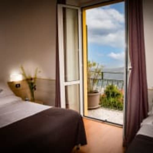 Camera dell'Hotel Vista Lago con balcone affacciato sulle montagne di Brunate, Italia. Letto, scrivania e vista della terrazza con vasi di fiori