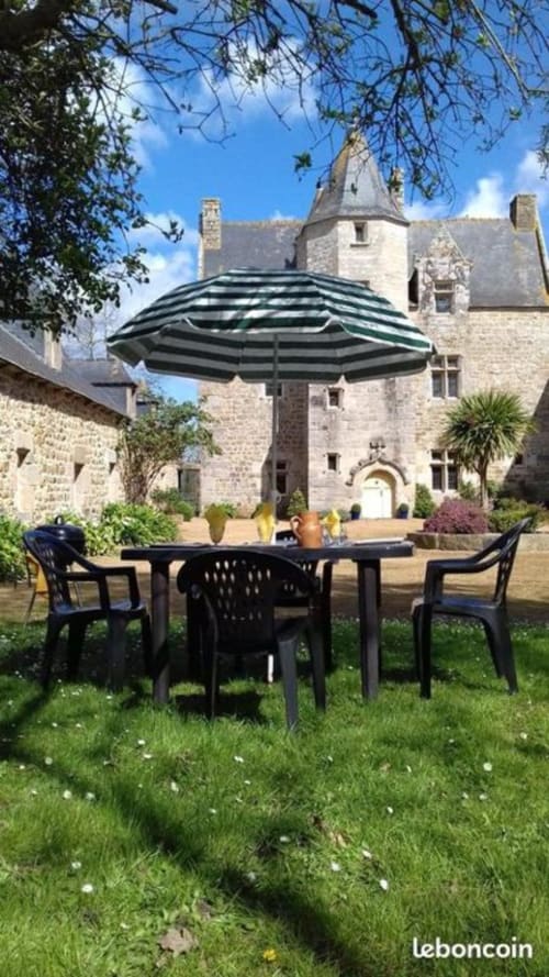 Table de patio noire avec parasol dans le jardin paysager du Manoir de Fornebello, château historique en pierre en arrière-plan