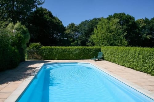 Piscine rectangulaire privée aux eaux turquoise, entourée d'une terrasse en pierre et de haies verdoyantes au Manoir de