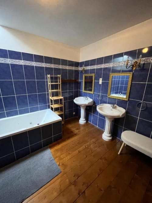 Suite de bain luxe au Manoir de Fornebello avec carrelage bleu marine, lavabos sur piédestal, baignoire et parquet