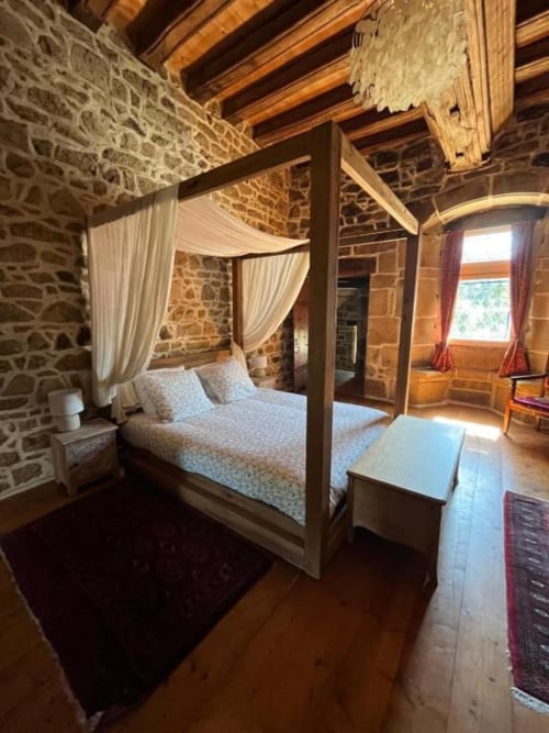 Lit à baldaquin élégant avec rideaux blancs dans la Suite Seigneuriale aux murs de pierre du Manoir de Fornebello