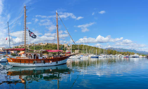 Traditional wooden sailboat docked in Porto-Vecchio harbor with mountains and blue sky