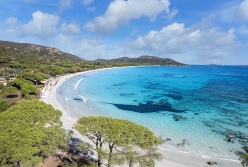 Pristine turquoise beach at Sweet Holiday, Porto-Vecchio, with white sand, clear Mediterranean waters, and lush hillside