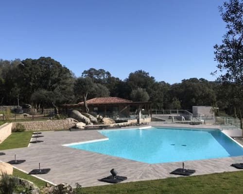 Sweet Holiday pool area in Porto-Vecchio with turquoise swimming pool, wooden deck, lounge chairs, and Mediterranean