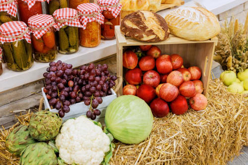 Fresh farm produce display at Sweet Holiday market: grapes, apples, vegetables, bread, and jarred preserves in Porto-Vecchio