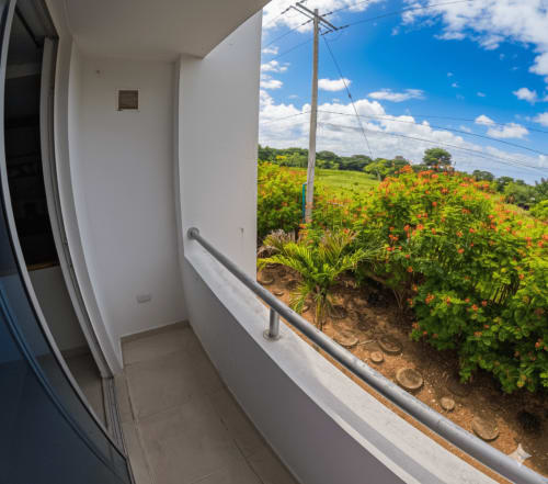 Vista del balcón de la habitación del hotel Olamar Living con vistas a un colorido jardín con flores y campos verdes en Coveñas, Colombia