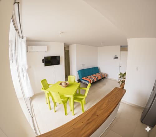 Luminoso salón de apartamento con mesa de comedor amarilla, sofá azul, TV de pantalla plana y comodidades modernas en Olamar Living