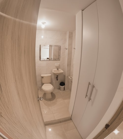 Baño moderno con inodoro, lavamanos, espejo y almacenamiento en el hotel Olamar Living de Santiago de Tolú, Colombia