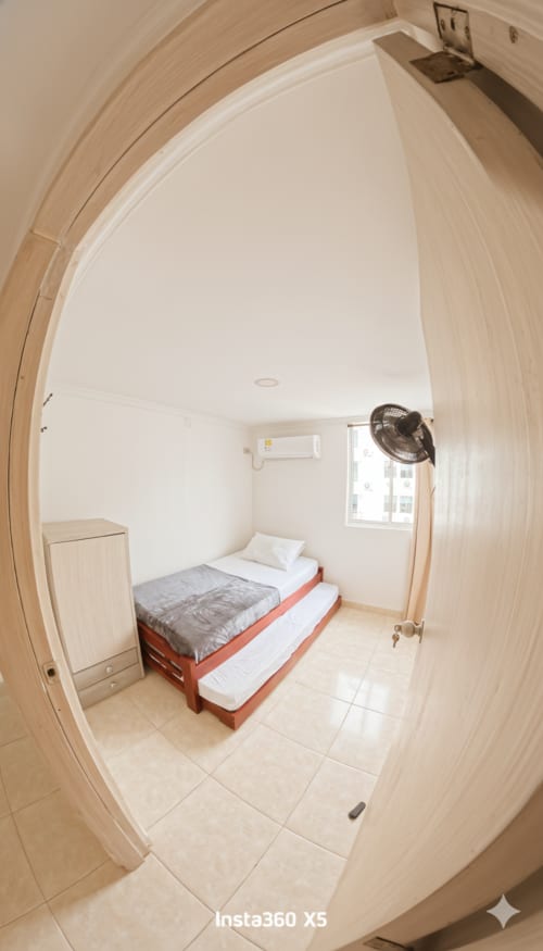 Habitación doble compacta en Olamar Living, Santiago de Tolú, con cama individual, armario, ventilador, aire acondicionado y vista por ventana