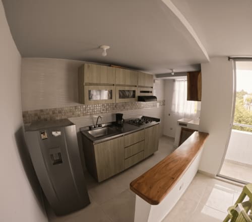 Cocina moderna con muebles de madera clara, estufa a gas, fregadero y mesón de comedor de madera en departamento Olamar Living, Santiago