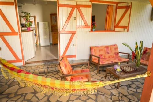 La terrasse colorée de la location Alpinia, avec son espace détente, son hamac, dans un jardin tropical fleuri. Aux jardins de Pointe Noire, en Guadeloupe