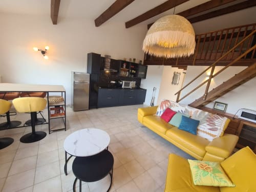 Bright open-plan living area with yellow furniture, black kitchen, and exposed wooden beams in Mana Bleu apartment managed by Corsu di Core