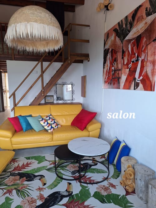 Colorful salon at Mana Bleu apartment with yellow sofa, tropical rug, and wooden staircase in Favone, managed by Corsu di Core