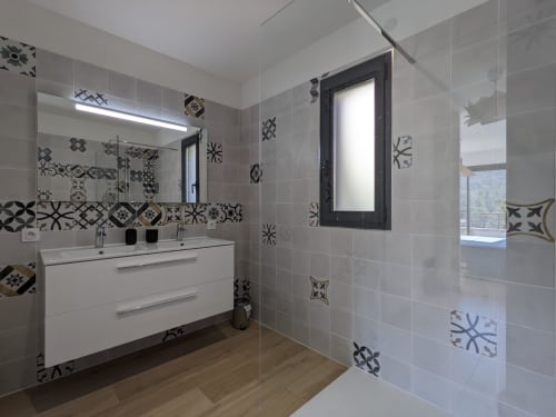 Modern bathroom at villa in Favone with decorative tile patterns, white vanity, and rainfall shower, managed by Corsu di Core