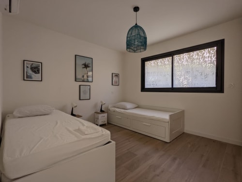 Modern shared bedroom in Villa Ô Bord de Mer, with two white beds, pendant light and framed artwork, managed by Corsu di Core