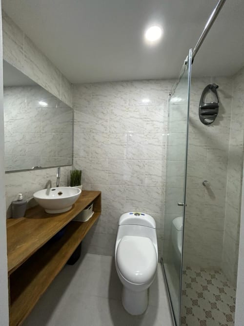 Baño moderno en Olamar Living con ducha de mármol, inodoro blanco, tocador de madera con lavabo redondo y techo luminoso