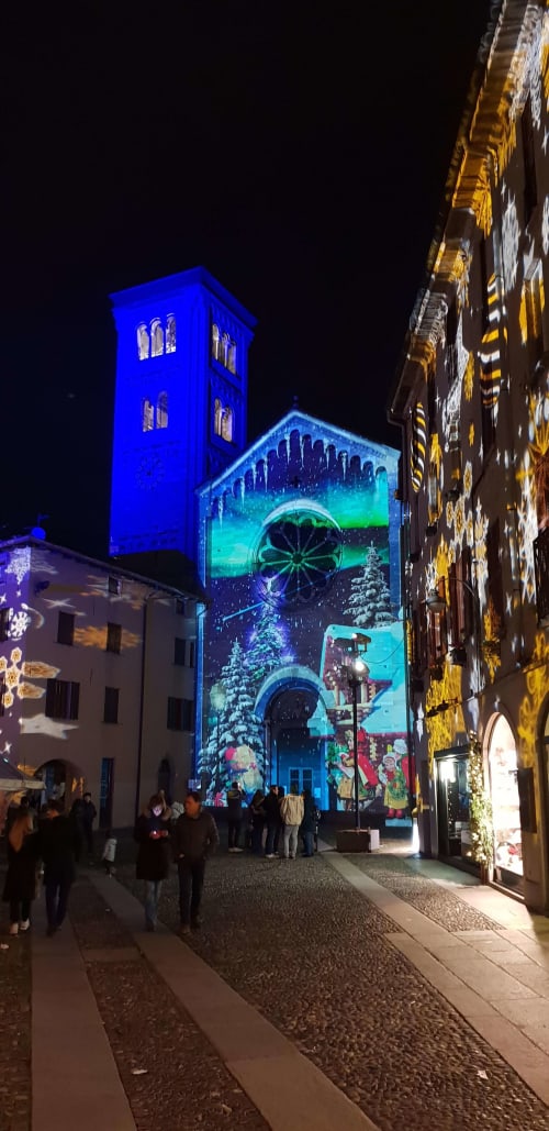 Historic church illuminated with blue and Christmas projections at night in Bellano, Como Lake region, Italy