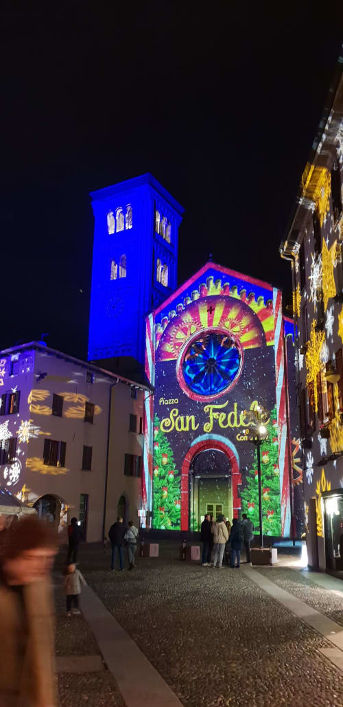 Colorful night projection on historic San Fede church in Bellano, Lake Como, with illuminated blue bell tower and festive