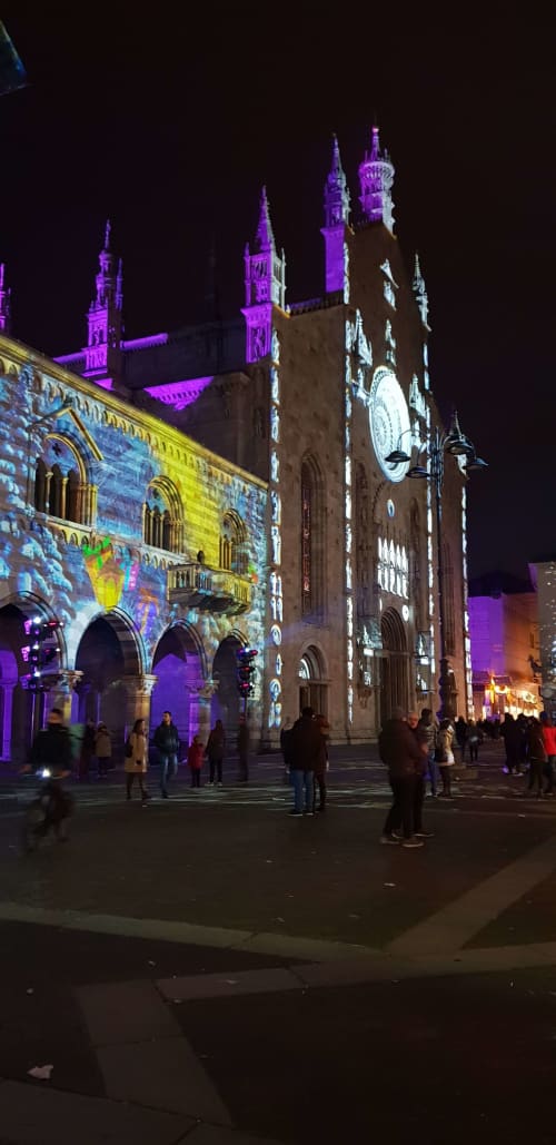 Gothic cathedral illuminated in purple at night with crowd gathering in plaza near Bellano