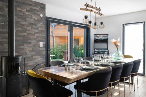 In diesem hellen und einladenden Esszimmer lädt ein großer Massivholztisch (für bis zu 10 Personen) zum Verweilen ein. Der Kaminofen sorgt für eine behagliche Atmosphäre, während die Flügeltüren auf einen ruhigen, privaten 400 m² großen Garten führen – ideal für Familien und Gruppen. Genießen Sie den Blick ins Grüne, die elegante Einrichtung (Samt, vergoldetes Metall) und den geselligen Raum, der sich perfekt für Abendessen, Brunch oder Besprechungen eignet.
