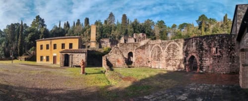 Cortile del Castagnini BnB con casa gialla, rovine storiche in pietra e cipressi a Montecatini Val di Cecina