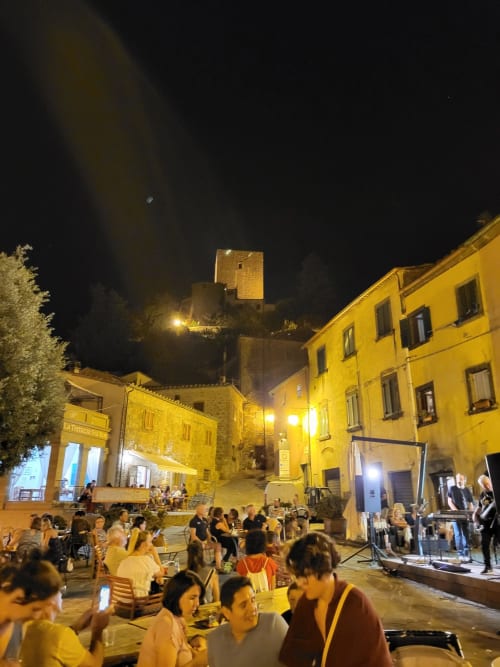 Evening gathering in Montecatini Val di Cecina piazza with illuminated historic tower and yellow buildings
