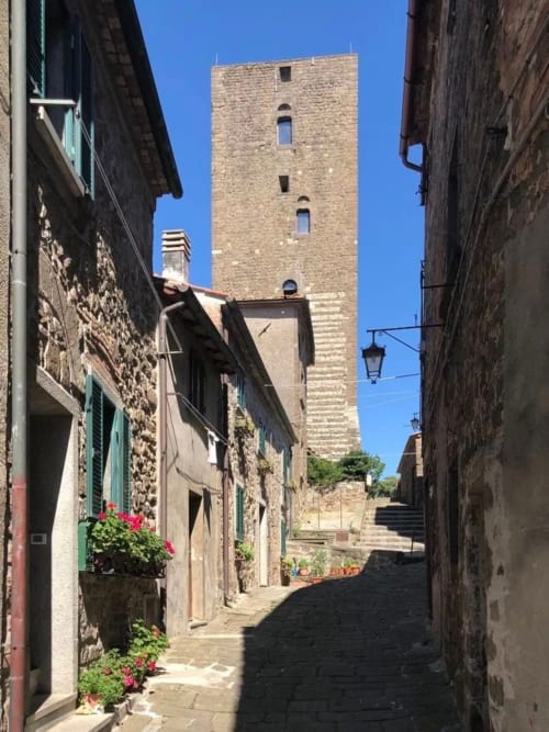 Narrow Italian village street lined with stone buildings leading to historic tower in Montecatini Val di Cecina