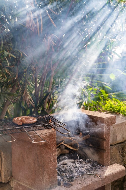 Outdoor brick grill with sizzling meat and smoke at Case Zucco B&B in Terrasini, Sicily