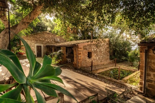 Rustic stone cottage at Case Zucco B&B in Terrasini, Italy, nestled among lush green trees and vegetation
