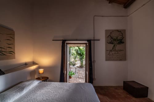 Bedroom at Case Zucco in Terrasini with bed, terrace doors opening to garden, warm lighting, and tree artwork