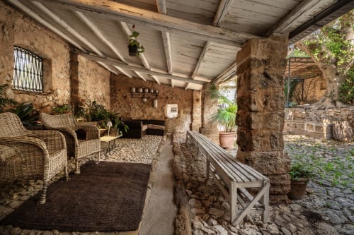 Rustic covered patio at Case Zucco B&B in Terrasini with wicker chairs, stone walls, and potted plants