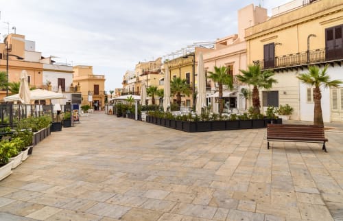 Terrasini town square with Mediterranean architecture, palm trees, and wooden bench at Case Zucco B&B