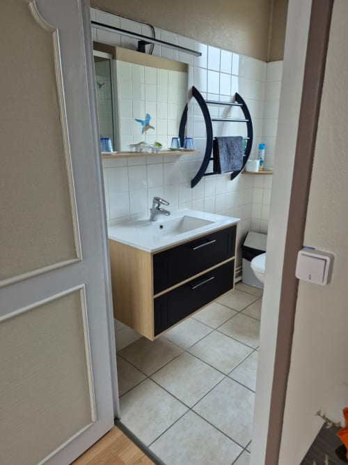 Salle de bains moderne avec meuble vasque en bois, lavabo blanc, grand miroir et porte-serviettes noir au Moulin Garnier B&B, Vernou sur