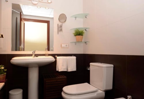 Baño moderno en apartamento de Mérida con lavamanos pedestal, inodoro y repisas de vidrio con plantas decorativas