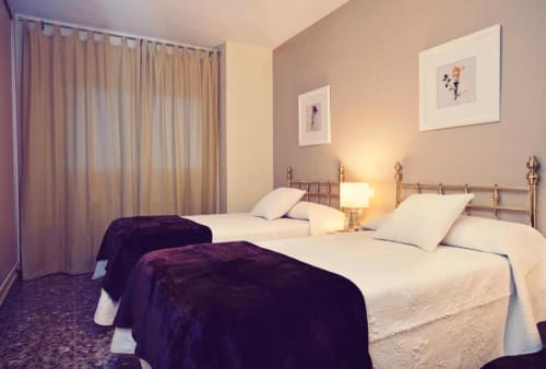 Dormitorio doble en apartamento Gestyp-AT, Mérida con camas de estructura metálica, ropa de cama color crema e iluminación cálida