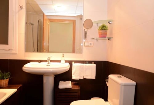 Baño moderno en apartamento de Mérida con lavamanos de pedestal, inodoro, espejo y estantes decorativos con plantas