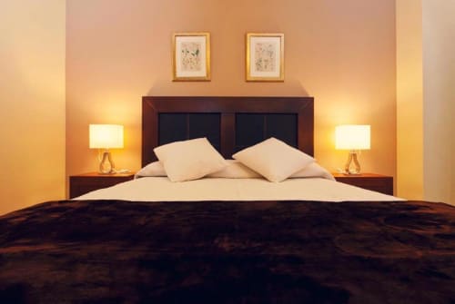 Dormitorio moderno en apartamento Gestyp-AT en Mérida con cama de madera oscura, almohadas crema, iluminación cálida y cuadros decorativos