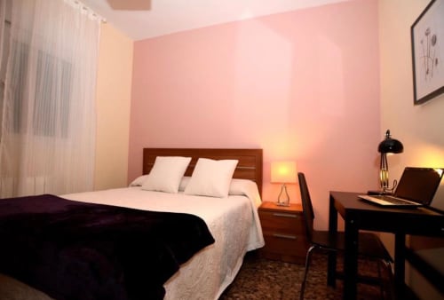 Acogedora habitación de apartamento en Mérida con pared de acento rosa, cama de madera, escritorio e iluminación cálida