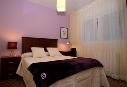 Moderno dormitorio con paredes de acento púrpura, cama de madera oscura y sábanas crema en el apartamento Gestyp-AT en Mérida