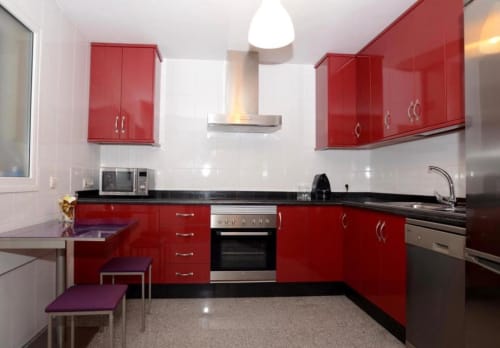 Moderna cocina roja con encimeras negras, electrodomésticos de acero inoxidable y comedor en apartamento de Mérida