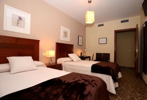 Habitación de hotel en Mérida con dos camas, cabeceras de madera, ropa blanca, detalles marrones e iluminación cálida.