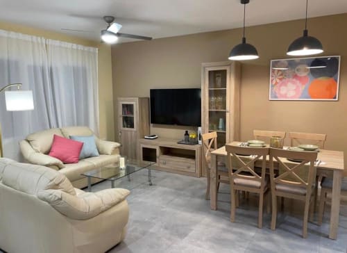 Amplia sala de estar en Mérida con sofás color crema, mesa de comedor de madera, televisor, lámparas colgantes y vistas a la ciudad