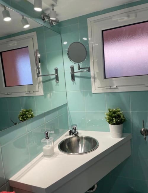 Baño moderno con azulejos turquesas, doble lavamanos y espejos redondos en la casa Gestyp-AT de Mérida