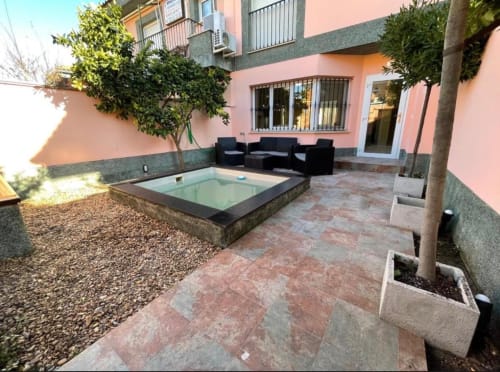 Patio de casa rural en Mérida con piscina pequeña, mobiliario negro, fachada rosa y patio arbolado