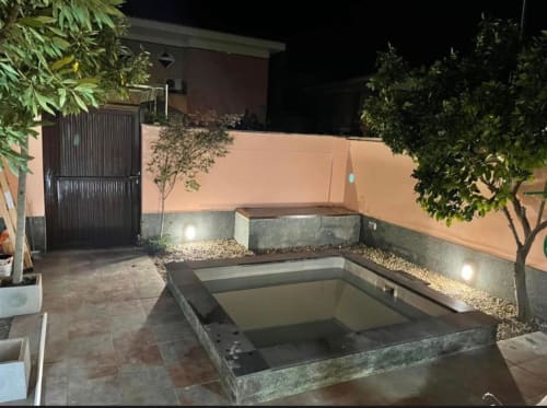 Área de spa exterior en la cabaña Gestyp-AT de Mérida con bañera de hidromasaje empotrada, iluminación ambiental y exuberante vegetación nocturna.