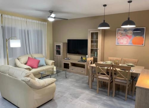 Zona de estar de cabaña moderna en Mérida con asientos color crema, mesa de comedor de madera, TV montado en pared e iluminación colgante