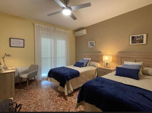 Habitación doble con vistas a la ciudad en la cabaña Gestyp-AT de Mérida, con dos camas con detalles azul marino, muebles de madera y