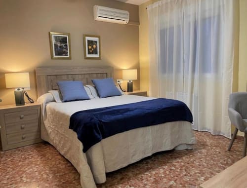 Dormitorio elegante en la posada Gestyp-AT de Mérida con acentos azules, ropa de cama neutral, lámparas laterales y vistas a la ciudad