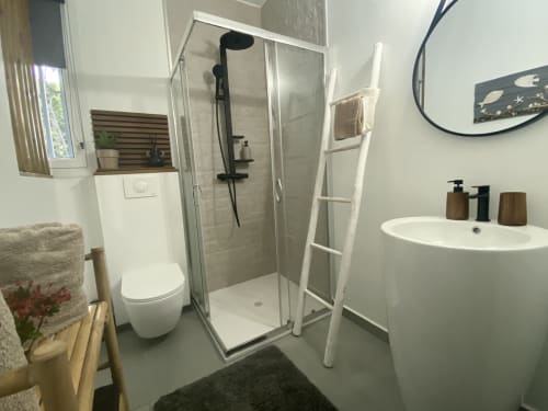 Chambre avec sa salle de bain moderne comprenant douche à l'italienne, vasque ronde, WC suspendus, porte serviettes et meuble de rangement bambou.